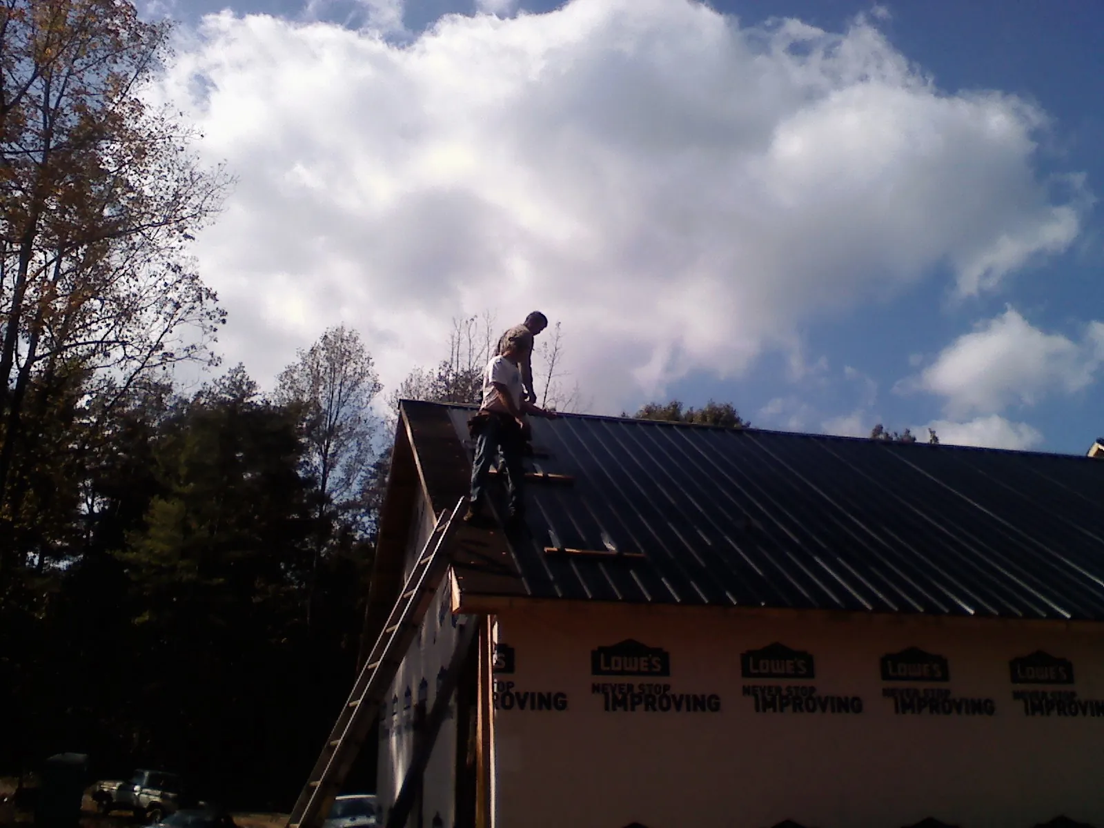 Roofer fastening dark metal panels high against a cloudy sky, from a Roof Inspection job in Culver City