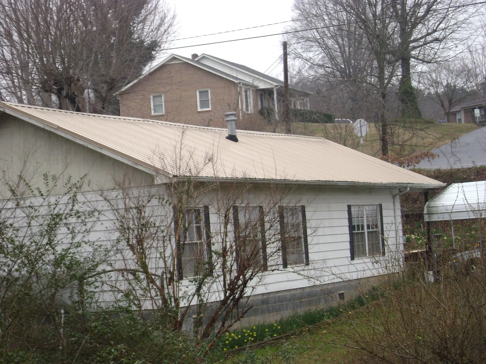 Tan metal roof on a white sided house set into a hillside — Commercial Roofing by Roofing Brothers in Culver City